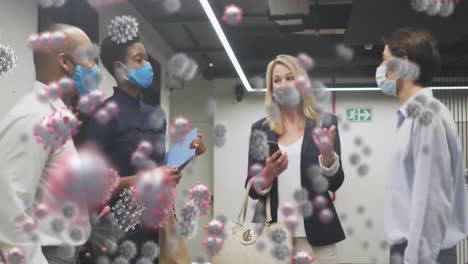 animation of covid-19 cells against diverse businesspeople wearing face masks discussing at office