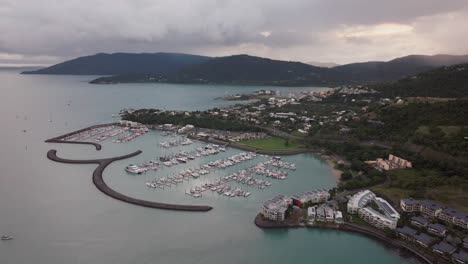 Port-Airlie-Beach-Bay-Lagoon-Coral-Sea-marina-aerial-drone-rain-clouds-mist-sunrise-morning-heart-of-Great-Barrier-Reef-Whitsundays-Whitehaven-jetty-yachts-sailboats-buildings-backward-motion