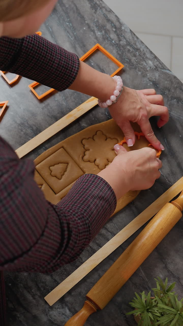 오렌지 카터를 사용하여 정확한 모양을 만들기 위해 굴러진 반죽을 사용하는 여성의 공중 사진, 베이킹 도구, 롤링 핀, 밀가루가 있는 나무 트레이가 인근에서 집에서 만든 페이스트리를 준비하는 장면을 설정합니다.