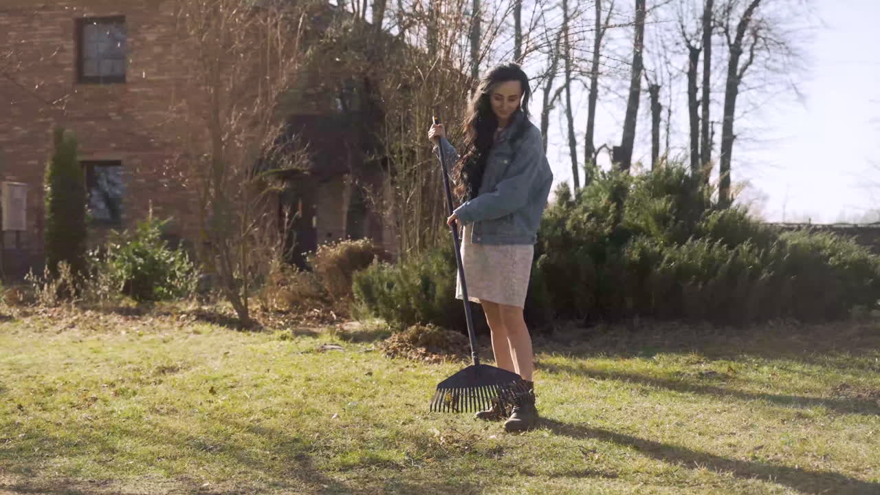 Caucasian woman removing weeds with a rake outside a country house