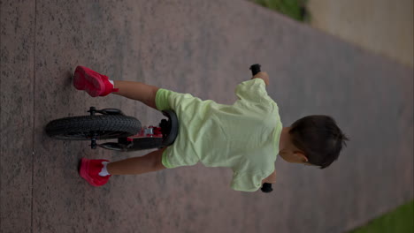 Vertikale-Zeitlupe-Eines-Jungen-Lateinamerikanischen-Jungen,-Der-An-Einem-Warmen-Nachmittag-Auf-Einem-Trainingsfahrrad-Fährt