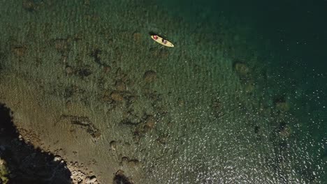 Vista-Aérea-Desde-La-Orilla-Del-Lago-Mientras-Los-Kayakistas-Pasan