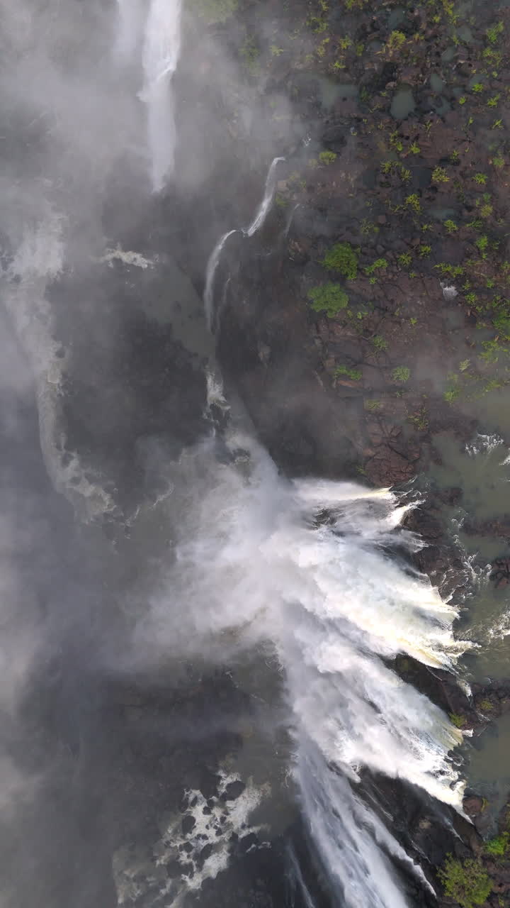 Aerial view of Victoria Falls with powerful waterfall plunging into gorge, mist rising above lush green forest, dramatic natural wonder and iconic travel destination in Africa - vertical Format