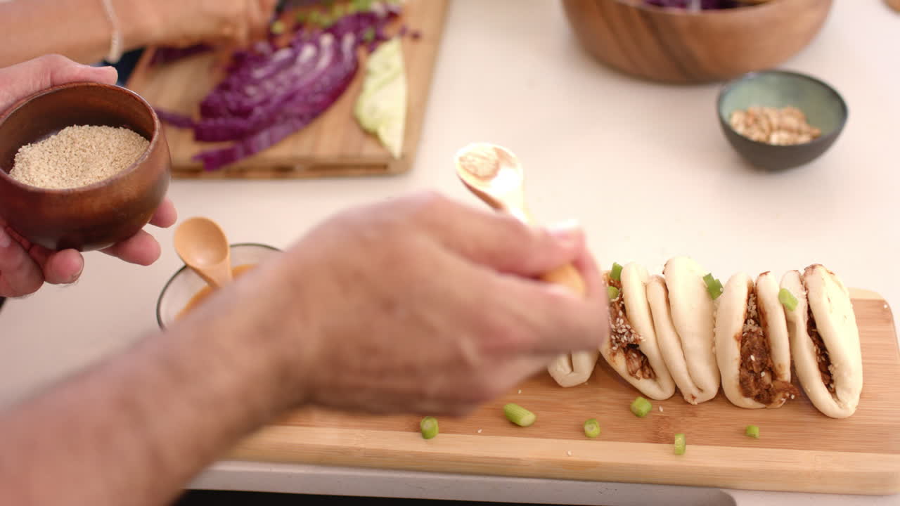 Sprinkling sesame seeds on bao buns, person preparing meal with vegetables
