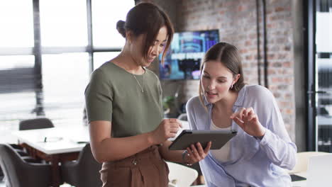 Young-Caucasian-woman-and-Asian-woman-review-business-content-on-a-tablet-in-an-office-setting