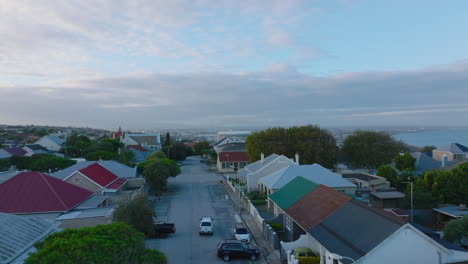 Residential-houses-with-colour-roofs-along-street-in-city.-Forwards-fly-above-urban-neighbourhood,-revealing-panoramic-view-of-town.-Port-Elisabeth,-South-Africa