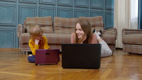 Woman-nanny-and-child-girl-studying-together-with-computer-laptop,-while-lying-on-warm-floor-at-home