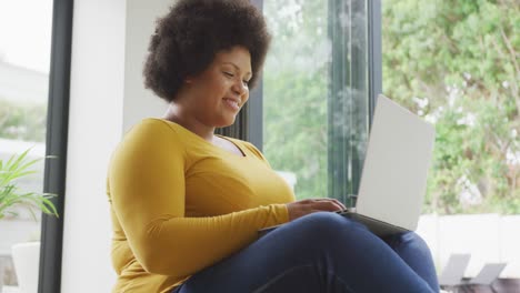 video of happy plus size african american woman sitting on floor and using laptop