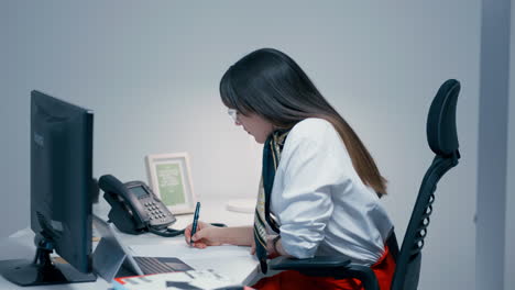 Hermosa-Joven-Con-El-Pelo-Largo-Y-Oscuro-Y-Gafas-Sentada-Detrás-Del-Escritorio,-Trabajando-Duro-En-El-Trabajo-En-La-Oficina-En-Cámara-Lenta