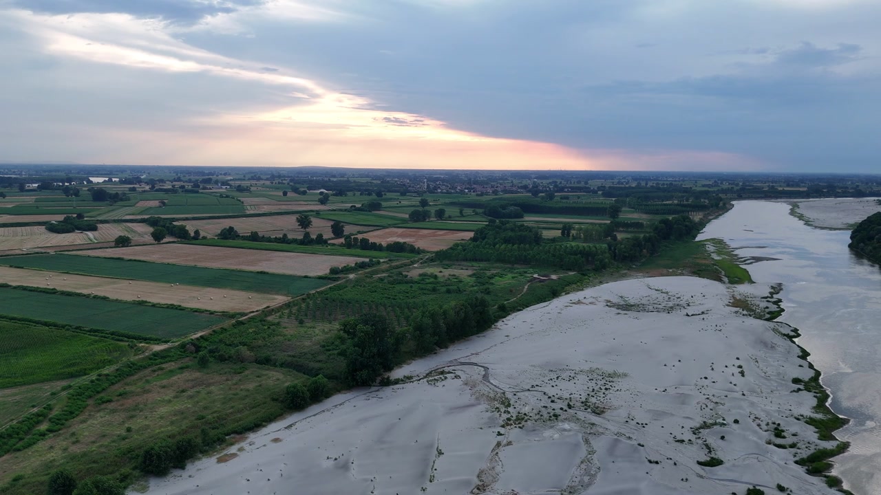 La siccità del fiume Po espone estese barre di sedimento pallido e canali poco profondi accanto a campi agricoli nella Pianura Padana del nord Italia, mostrando gravi condizioni di bassa marea, ripresa aerea con drone