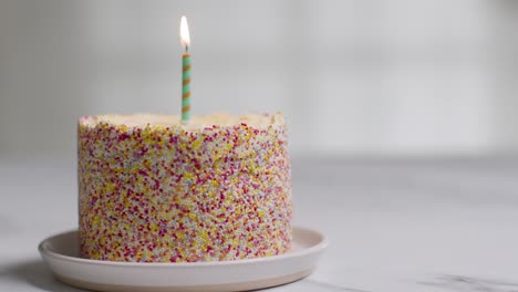 single candle being blown out in studio shot of birthday cake covered with decorations 2