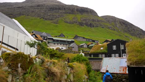 turista masculino explorando el pueblo de bour con casas de techo de césped y montañas volcánicas en las islas feroe