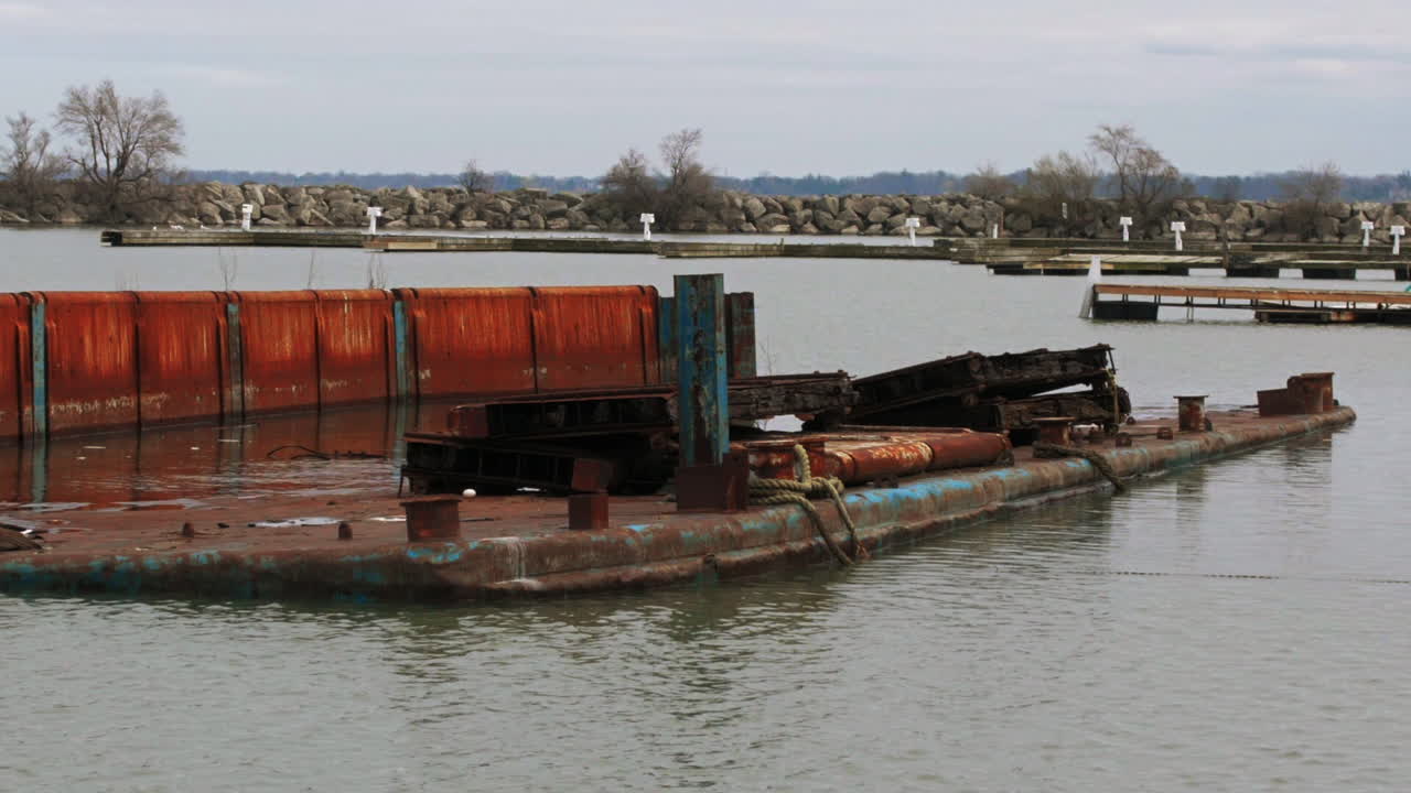 Floating rusted red metal barge in shallow green waters