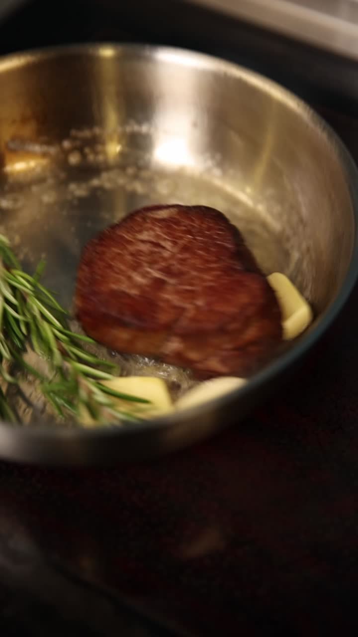 Steak being cooked in a pan with butter, garlic, and rosemary