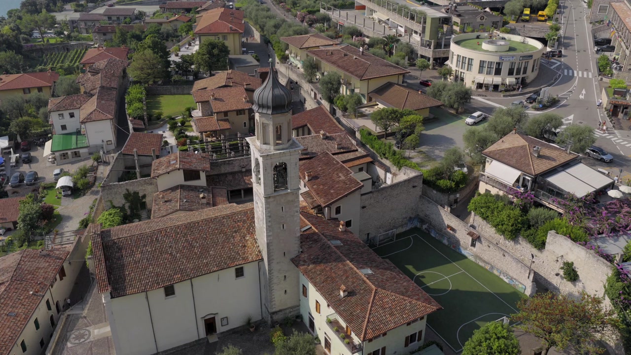 Aerial drone footage transitioning from top-down view to horizontal perspective of a church in Limone sul Garda, with Lake Garda and surrounding mountains creating a scenic backdrop.
