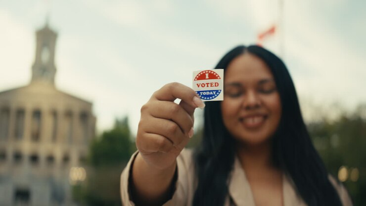 Woman holding 'I Voted' sticker in front of government building