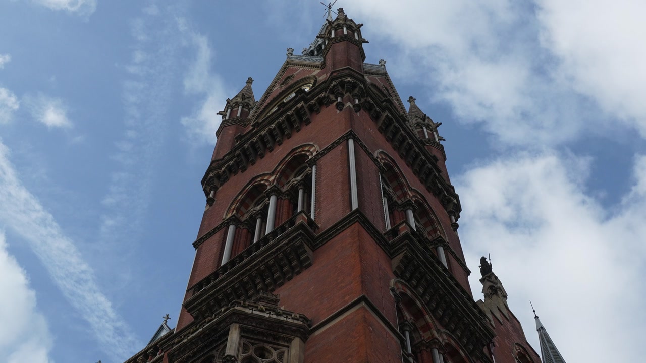 Low angle view of the ornate red brick Gothic tower of the St Pancras Renaissance Hotel in London against a partly cloudy sky. Dramatic architectural detail showcasing Victorian design and historic