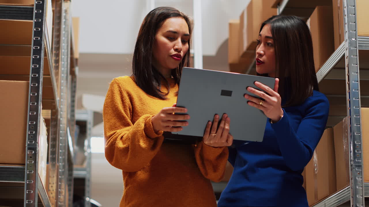 Two women using a laptop in a warehouse