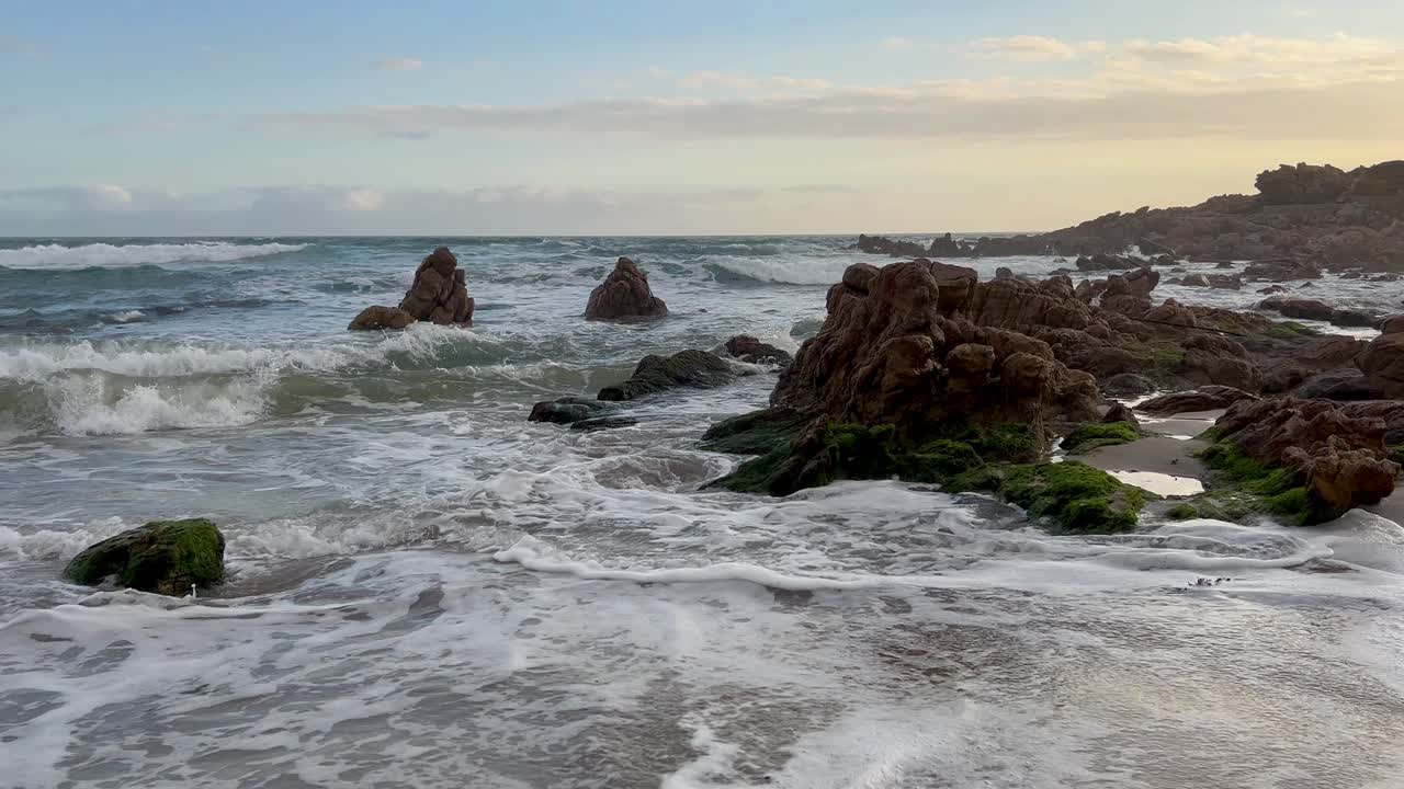 Le onde si infrangono e si ritirano su una spiaggia durante un meraviglioso tramonto