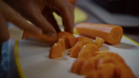 man cutting slice of carrot in kitchen at home. healthy diet food. young male chopping carrots on cutting board. guy prepares food in kitchen. he chopping carrot at home. practices cooking.