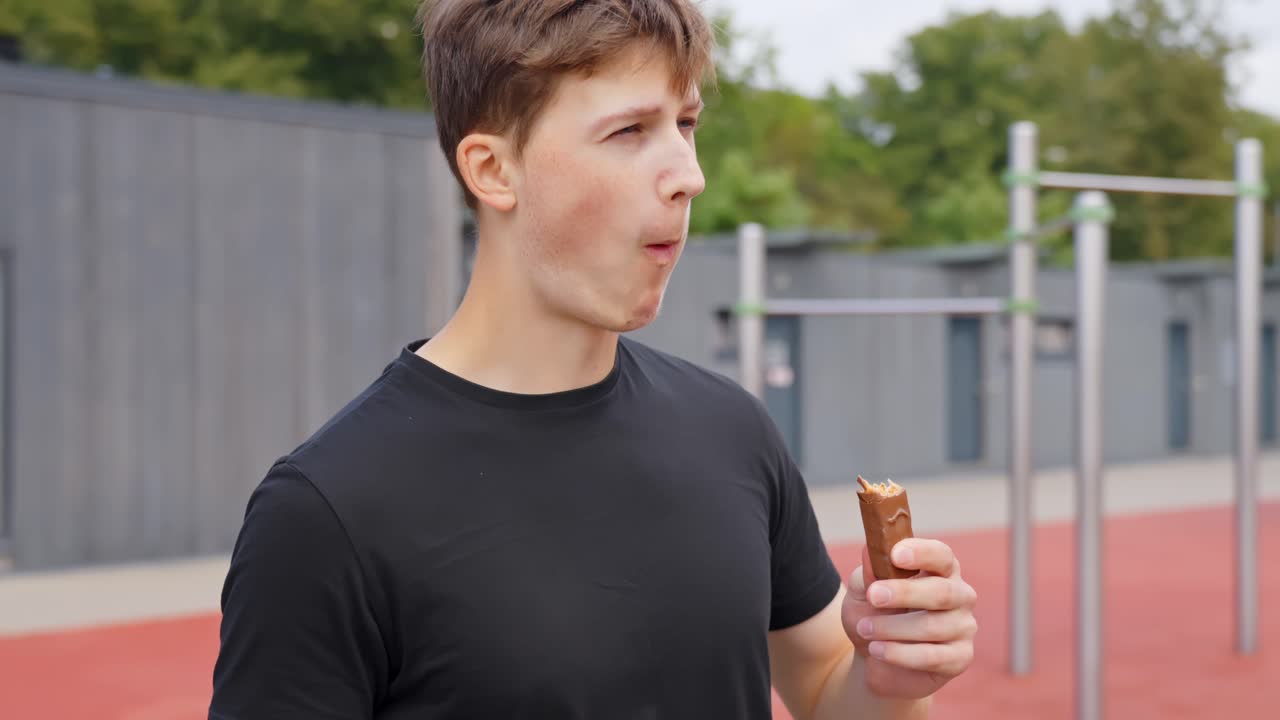 Young athlete eating a protein bar to refuel after a workout at an outdoor gym