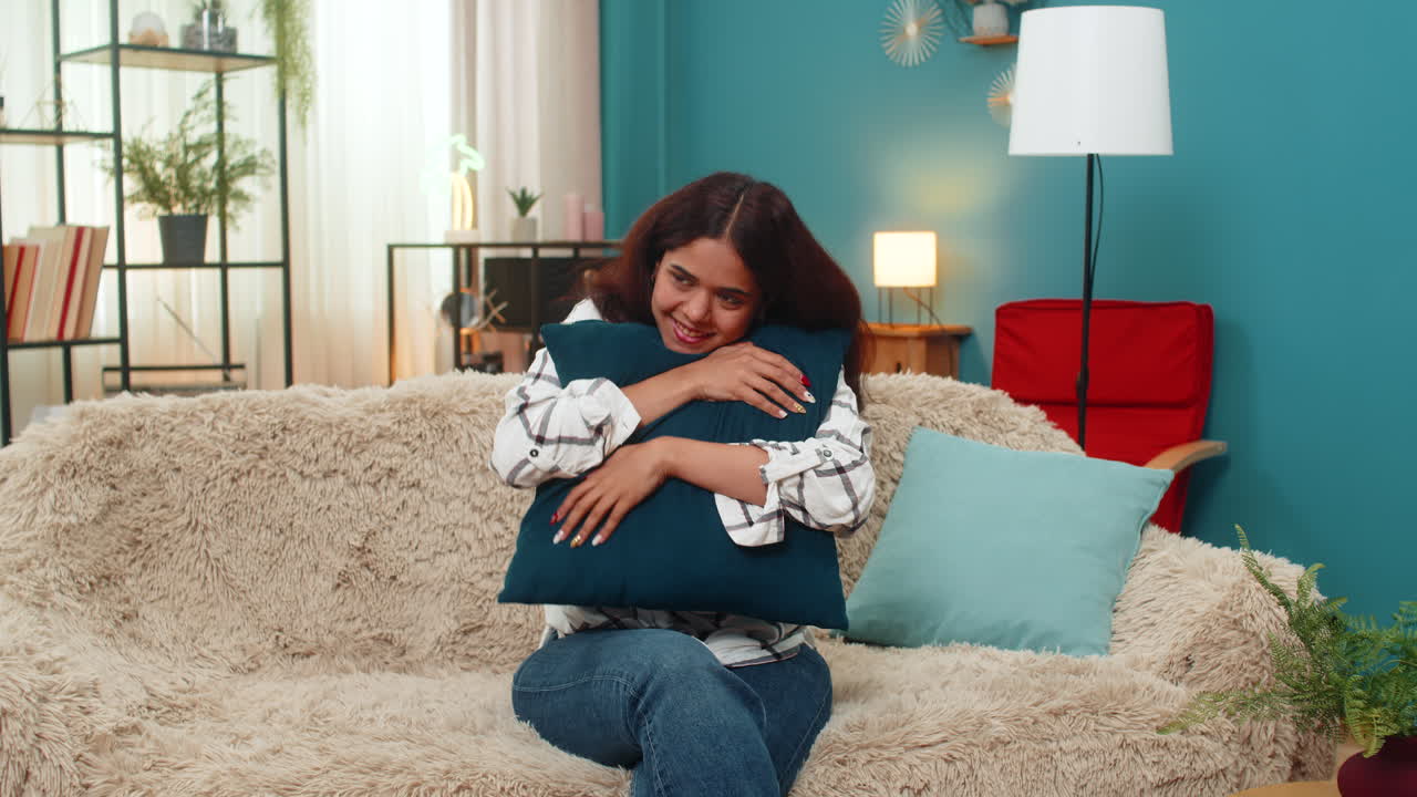 Indian woman playful mood tosses pillow upward catches smile joyful carefree indoor fun leisure shot