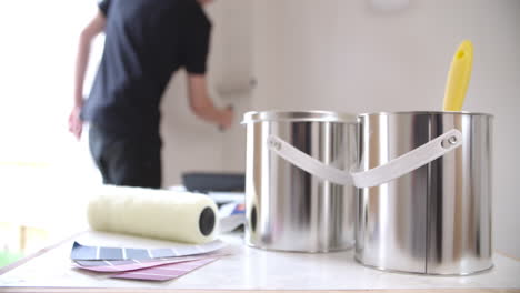 Man-painting-wall-with-paint-roller,-paint-in-the-foreground