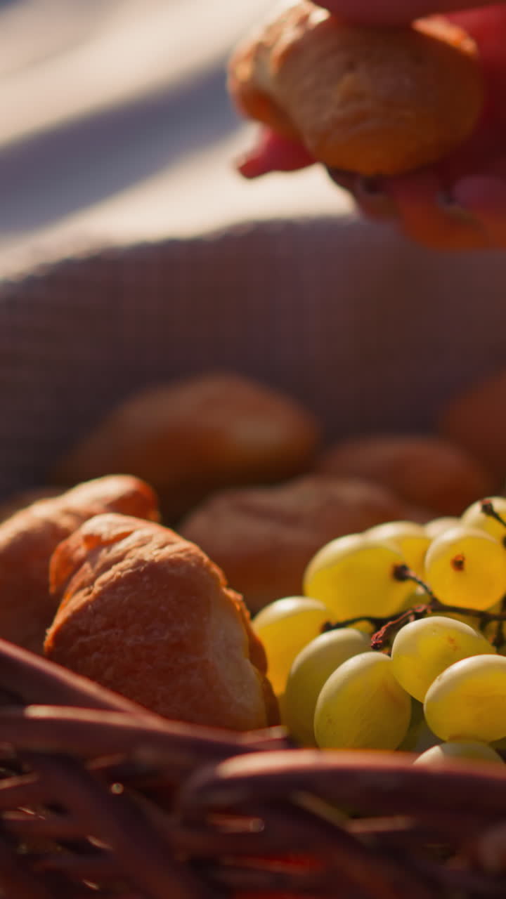 mujer toma pan horneado de la canasta de comida. realizando un picnic con frutas saludables y productos de harina en la playa en un clima soleado. relajación y saciedad del hambre