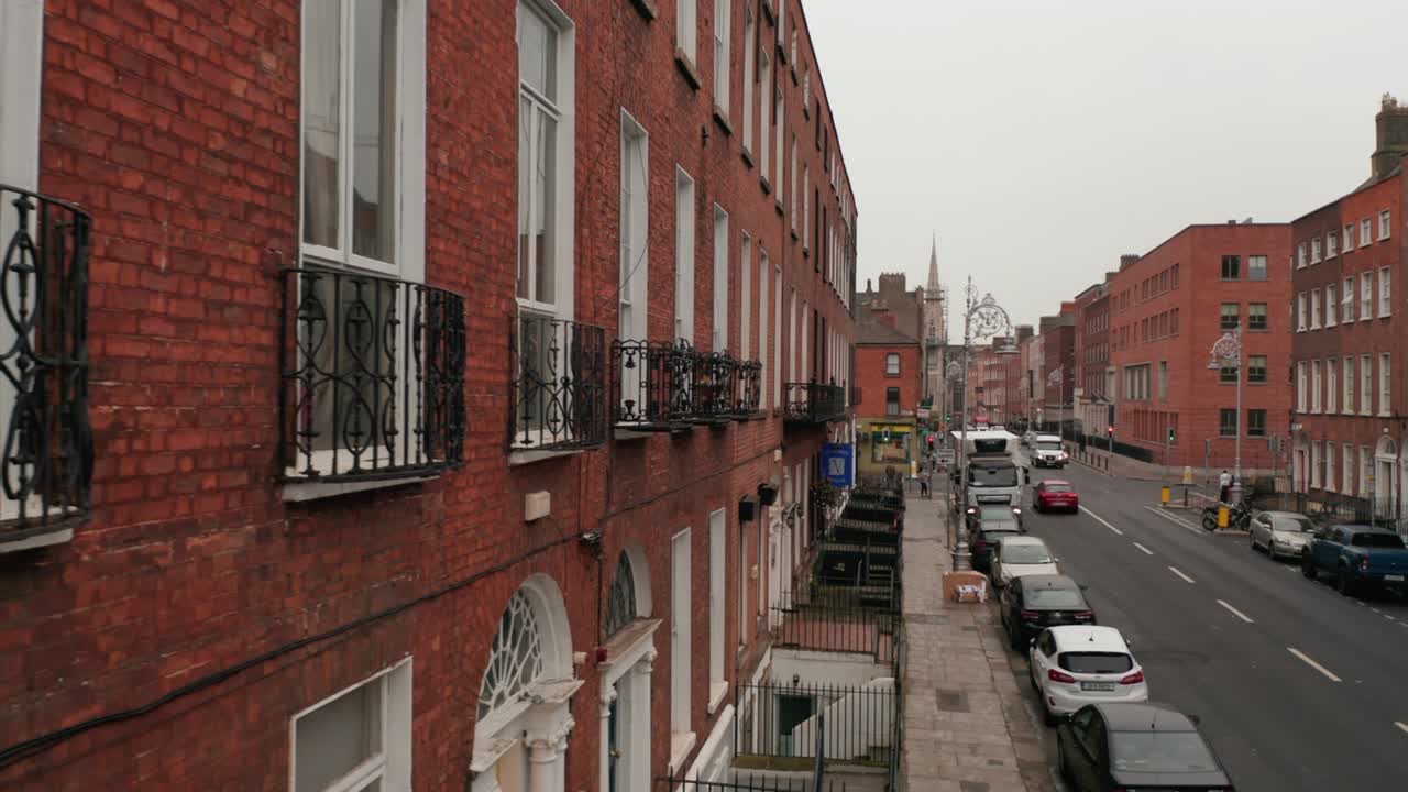 벽돌로 된 집 벽에서 끝에 교회가 있는 은 거리의 중앙으로 슬라이더. 도로를 따라 주차된 자동차. 더블린, 아일랜드