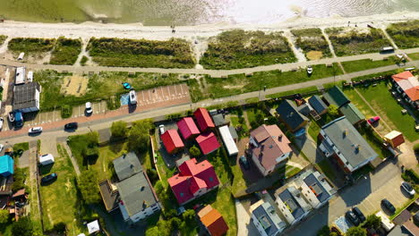 Top-down-aerial-view-of-Kuźnica-showing-a-row-of-buildings-with-red-roofs-adjacent-to-a-parking-area,-with-a-natural-dune-landscape-leading-to-the-shoreline