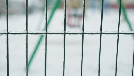primer plano de una valla metálica verde cubierta de hielo transparente, con helados individuales que se forman en los cables, en un fondo nevado borroso