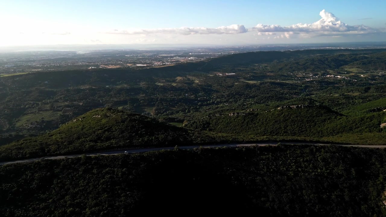 Vista aérea sobre estrada sinuosa e colinas verdes exuberantes sob a luz do sol da tarde.