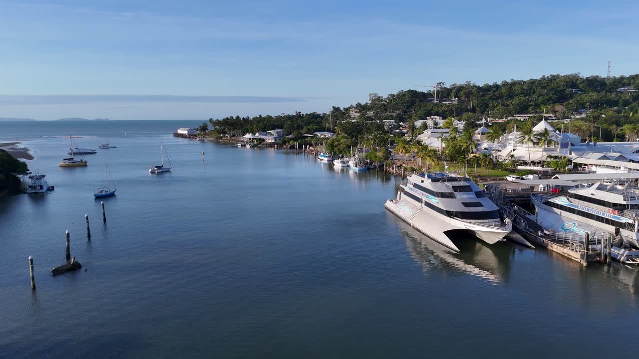 Drone footage captures a serene marina with boats in Port Douglas, Australia, under clear skies and calm waters