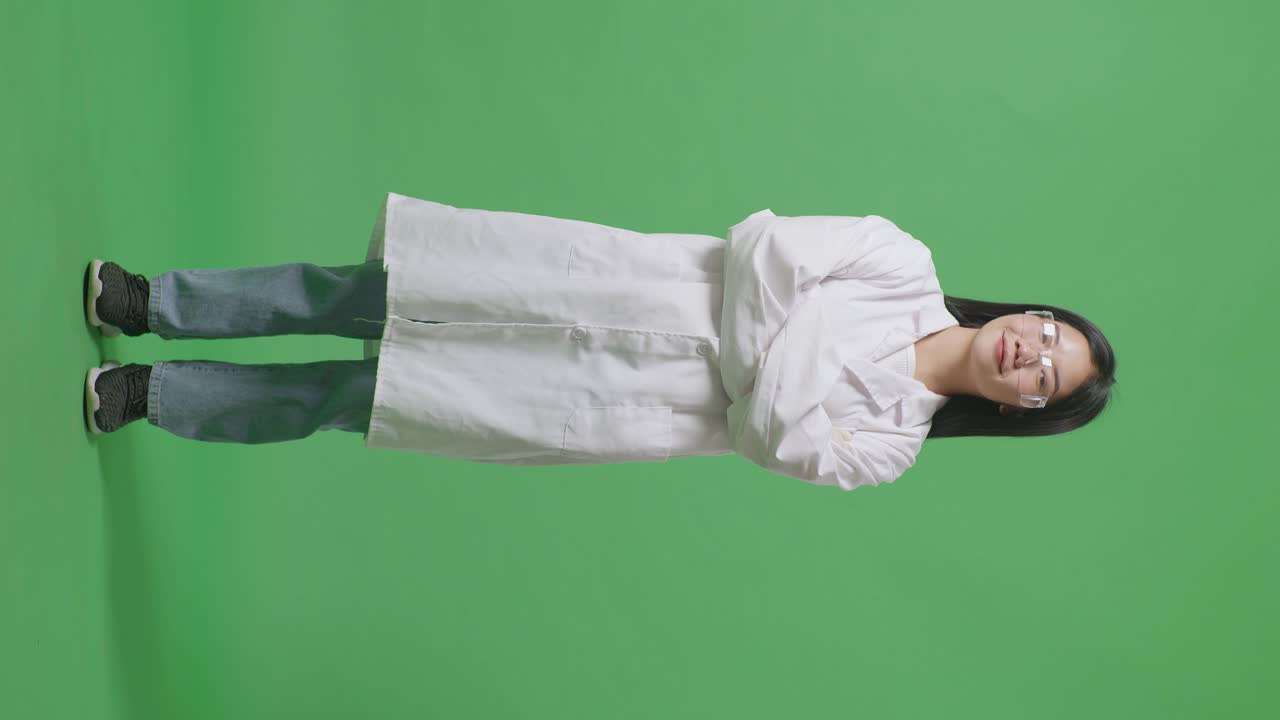 아시아 여성 과학자가 미소 짓고 팔을 는 채 실험실의 녹색 화면 배경에 서 있습니다.