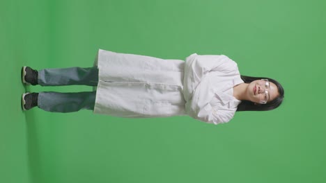 아시아 여성 과학자가 미소 짓고 팔을 는 채 실험실의 녹색 화면 배경에 서 있습니다.