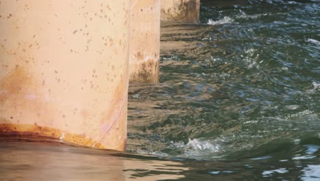 orange concrete bridge pilings with river water current rushing past