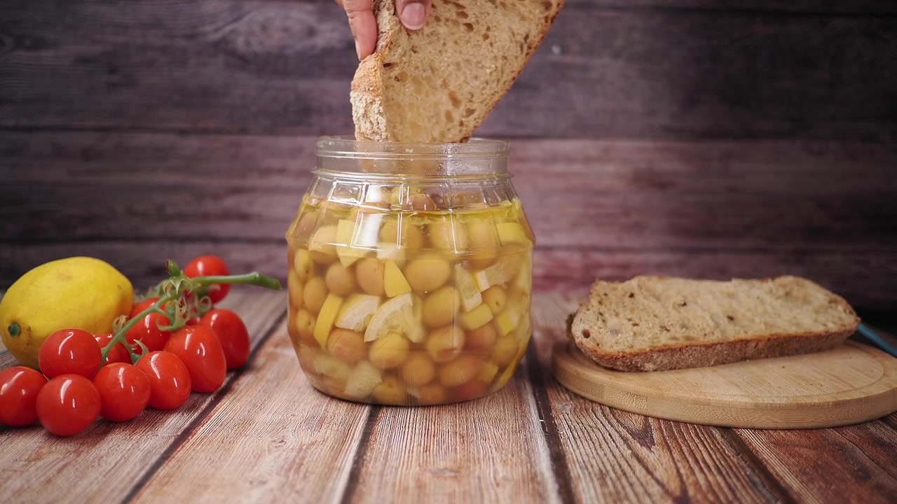 Persona che intinge il pane in un barattolo di olive marinate