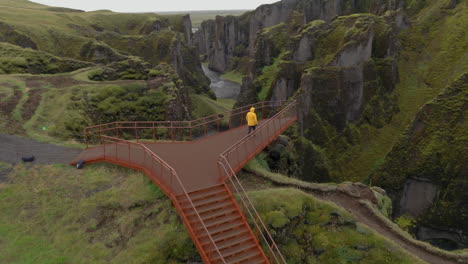 Aerial:-One-man-with-yellow-jacket-walks-on-the-platform-towards-the-Fjadrargljufur-Canyon-in-Iceland