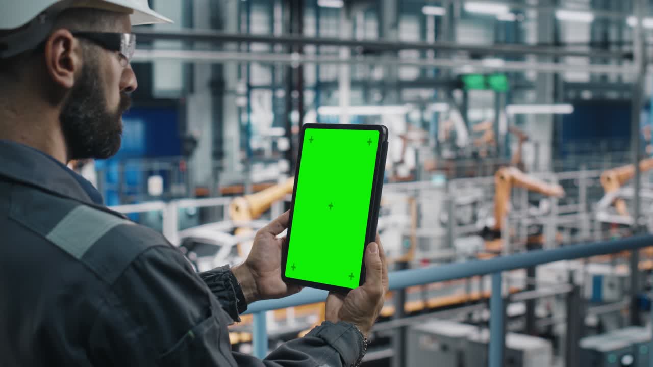 작업 유니폼을 입은 자동차 공장 엔지니어가 녹색 화면 모 디스플레이를 가진 태블릿 컴퓨터를 사용하여 자동차 산업 제조 시설에서 차량 생산을 위해 작업하는 증강 현실 소프트웨어를 사용합니다.