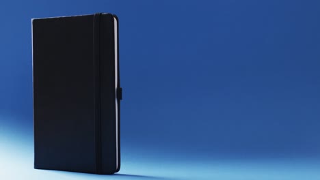 closed black notebook standing vertical with copy space on blue background in slow motion