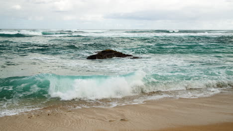 churning moody, dark waves over dark rock on beach in slow motion