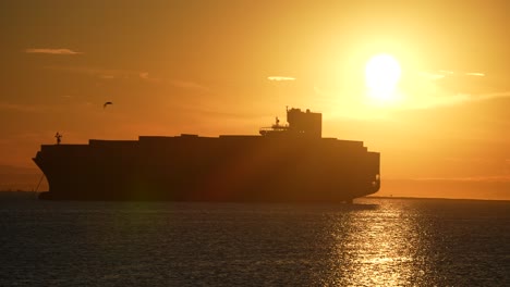 silhouette of a huge container cargo freight ship docked in the harbor during a global supply chain crisis during a golden sunset