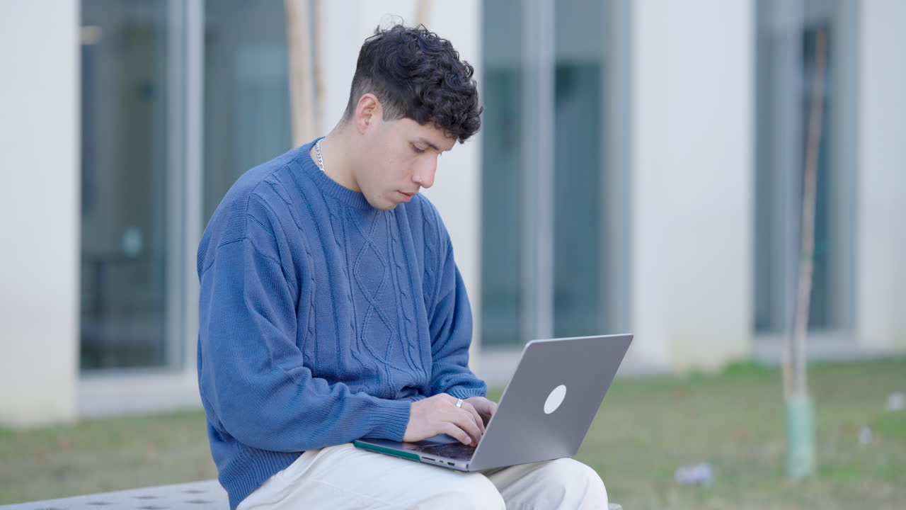 Young man sitting in college campus and using laptop