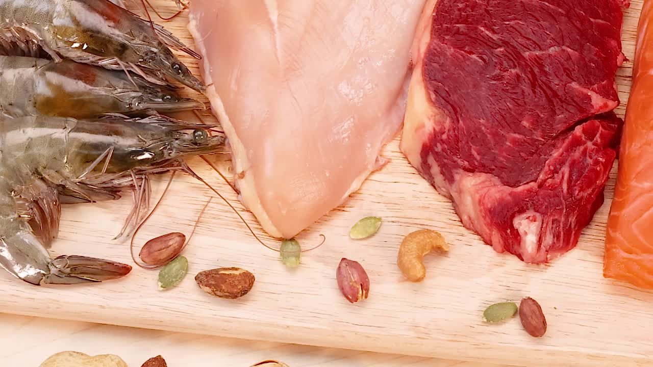 Una varietà di fonti proteiche, tra cui gamberi, pollo, manzo e salmone, disposte con noci su un tagliere di legno.