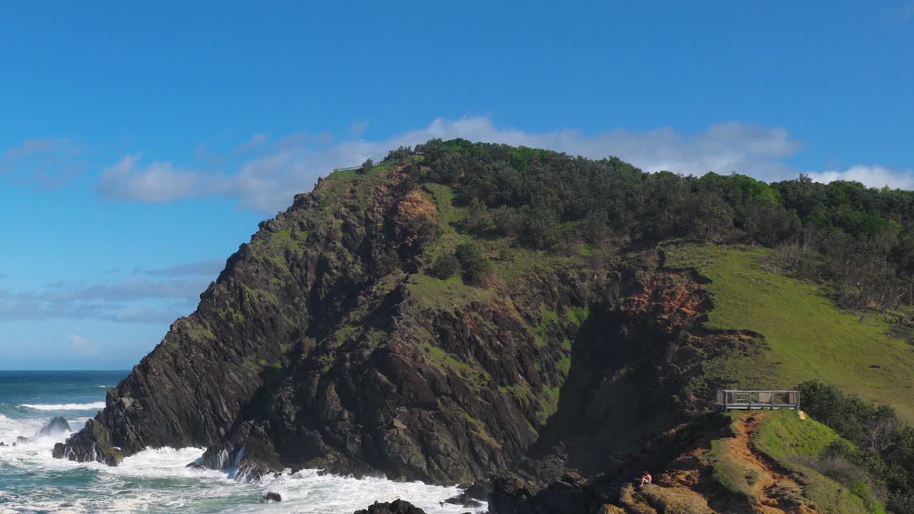 Dynamic ocean waves crash against a rugged cliff under a bright blue sky at Byron Bay, Australia