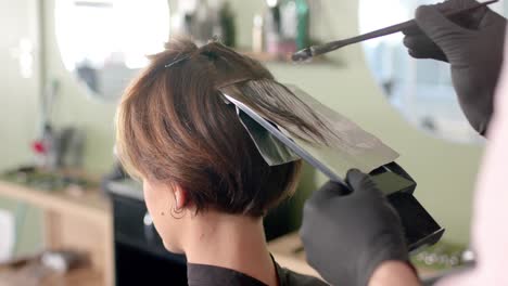 hands of hairdresser highlighting client's hair with brush and foil at hair salon, in slow motion