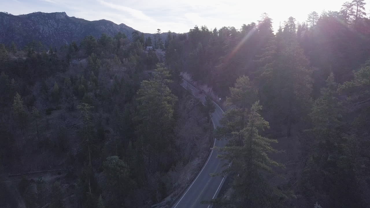la carretera de dos carriles serpentea a través de un bosque de pinos de montaña con una gama en el fondo