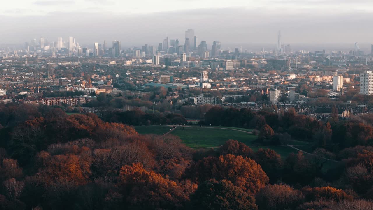 Circling drone backs away from Parliament Hill, London, showing full expanse of fall-colored trees, aerial establishing