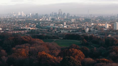 Circling drone backs away from Parliament Hill, London, showing full expanse of fall-colored trees, aerial establishing
