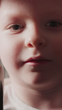 serious blond boy holds heavy barbell in hands looking in camera. cute toddler prepares for exhaustive workout in modern gym closeup slow motion